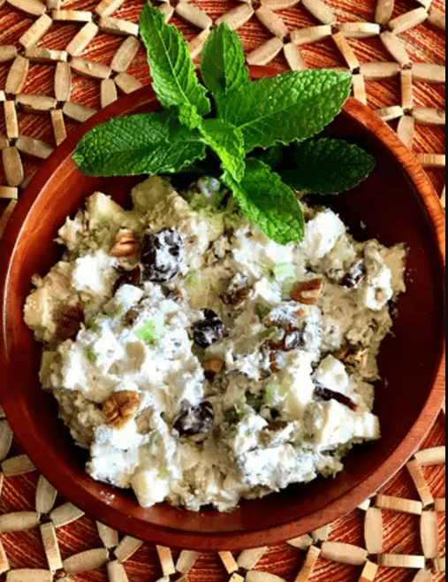 Refreshing walnut and raisin chicken salad served in a terracotta bowl garnished with fresh mint leaves, on a woven mat background