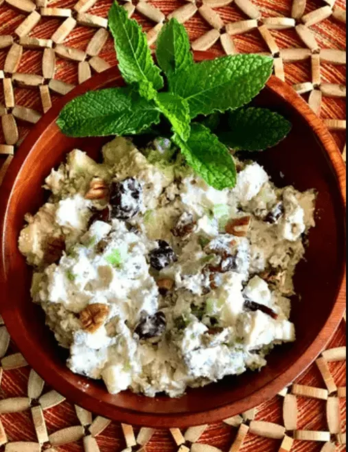 Healthy Chicken Recipes: Refreshing walnut and raisin chicken salad served in a terracotta bowl garnished with fresh mint leaves, on a woven mat background