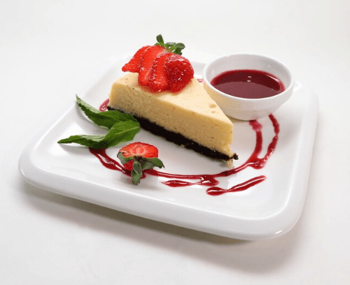 Slice of sugar-free cheesecake with almond flour crust, topped with fresh strawberries and blueberries on a white plate.