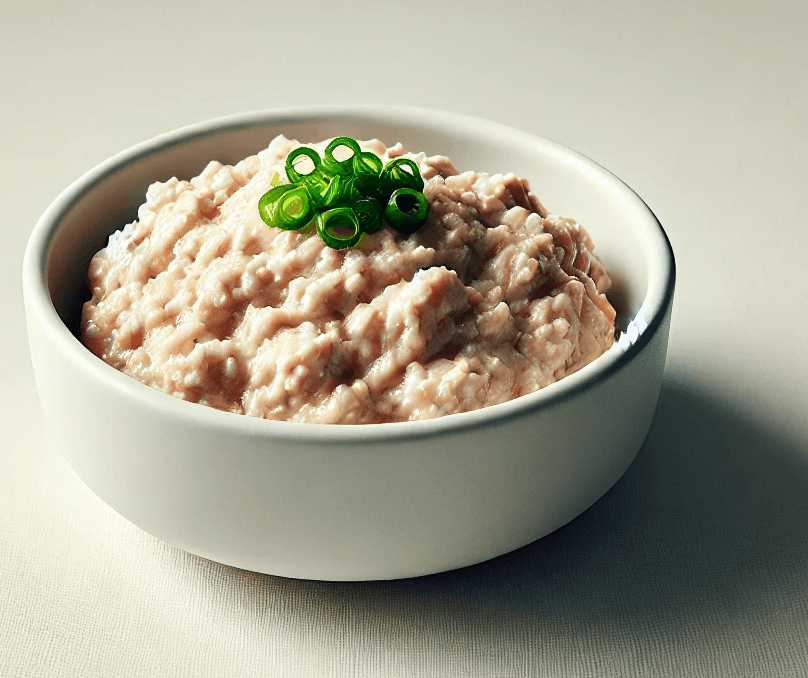 Simple white bowl with velveted ground chicken, garnished with green onions on a plain background