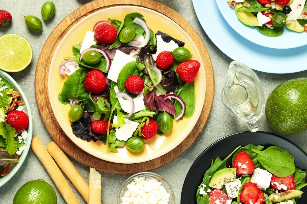 Fresh and colorful mixed green salad with strawberries, avocado, feta cheese, and lime, displayed on vibrant plates with healthy toppings.