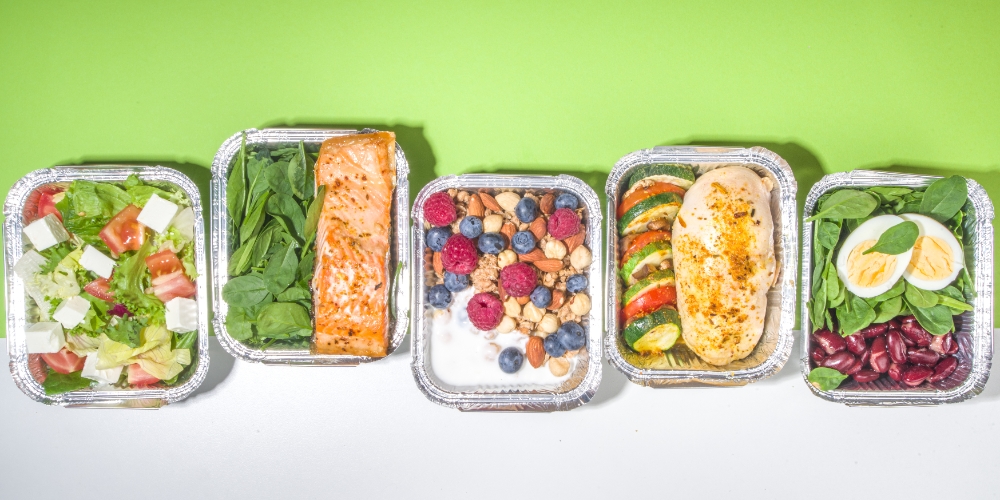 A colorful display of healthy meal prep containers featuring 30g protein lunches, including grilled chicken, salmon, boiled eggs, beans, salads, and Greek yogurt with berries.