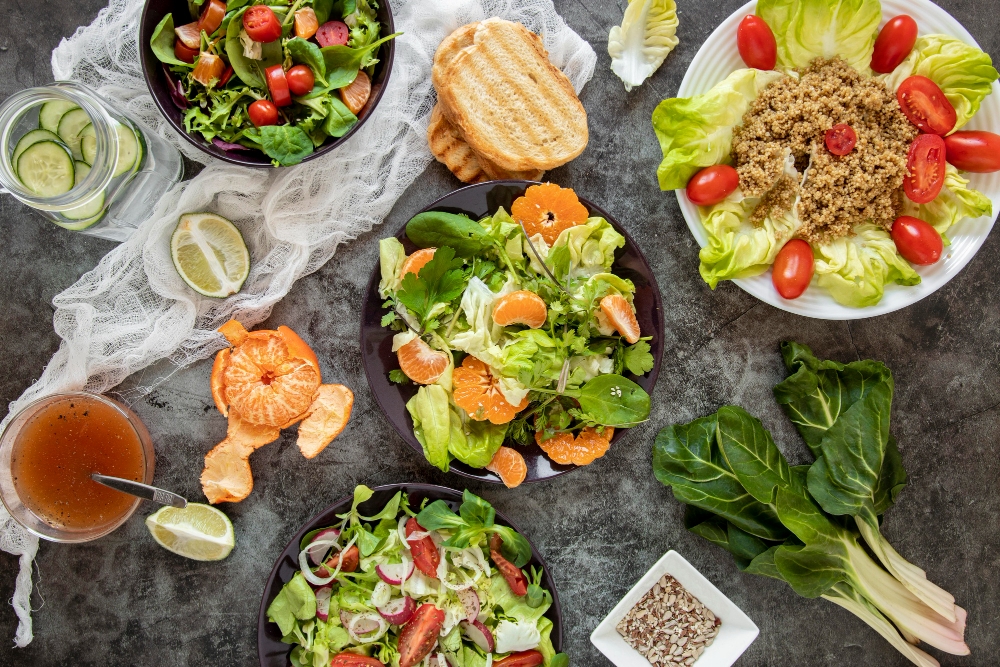 A variety of fresh salads featuring leafy greens, quinoa, cherry tomatoes, mandarin slices, and a side of bread, presented on a rustic table. Top 10 Healthy Lunch Ideas