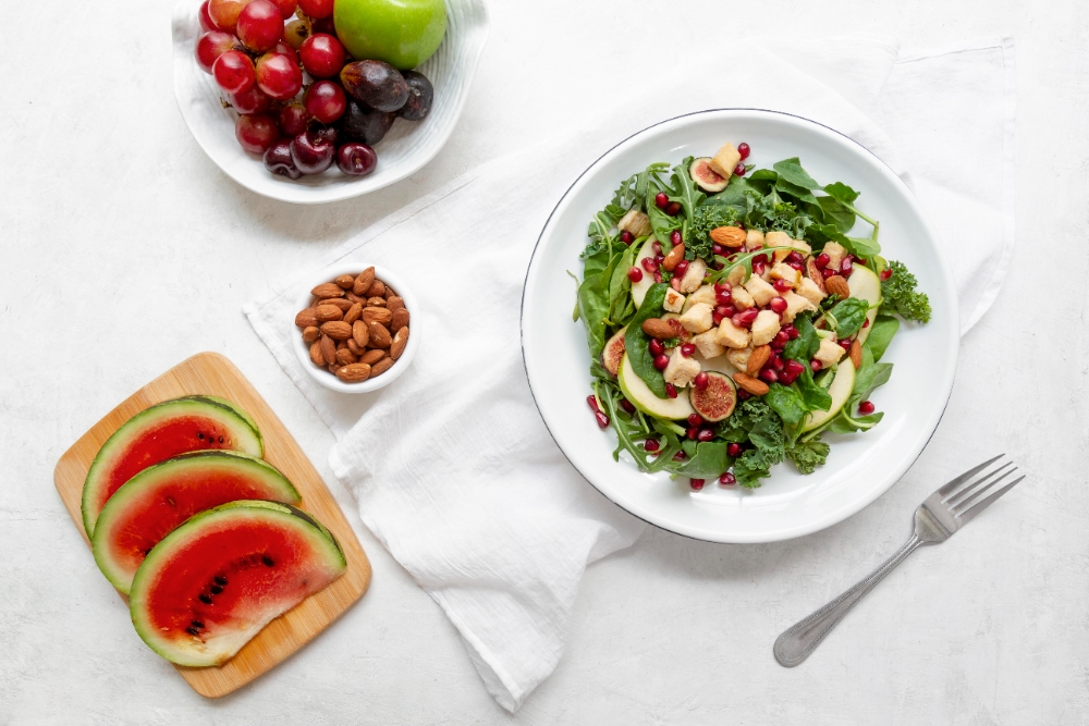  Fresh green salad with apple slices, pomegranate seeds, figs, almonds, and a side of fruits and watermelon slices on a wooden board