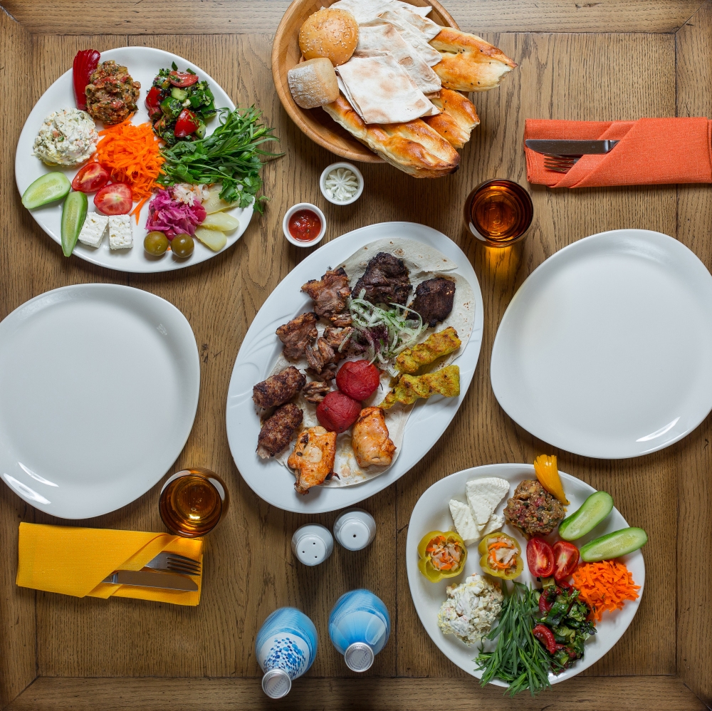  "Traditional Mediterranean meal with grilled meats, fresh vegetables, salads, and bread served on a wooden table."