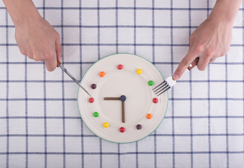 A creative clock design made from colorful food items on a plate, with hands using a knife and fork, symbolizing quick meal preparation.