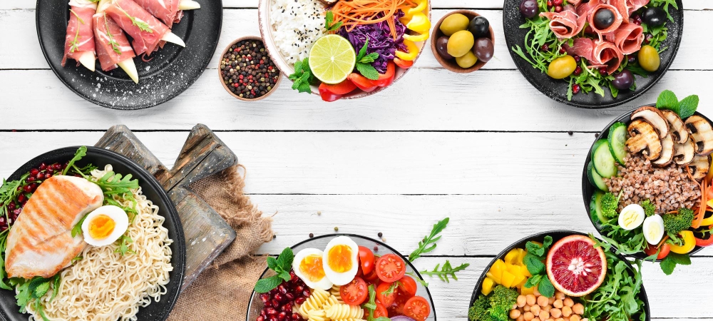  A variety of 30g protein lunch bowls featuring grilled chicken, boiled eggs, fresh salads, chickpeas, vegetables, and healthy grains, arranged on a white wooden table.