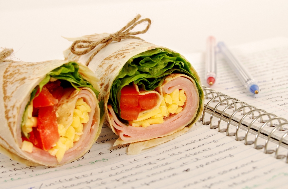 Healthy breakfast wrap with scrambled eggs, ham, lettuce, and tomato in a tortilla.