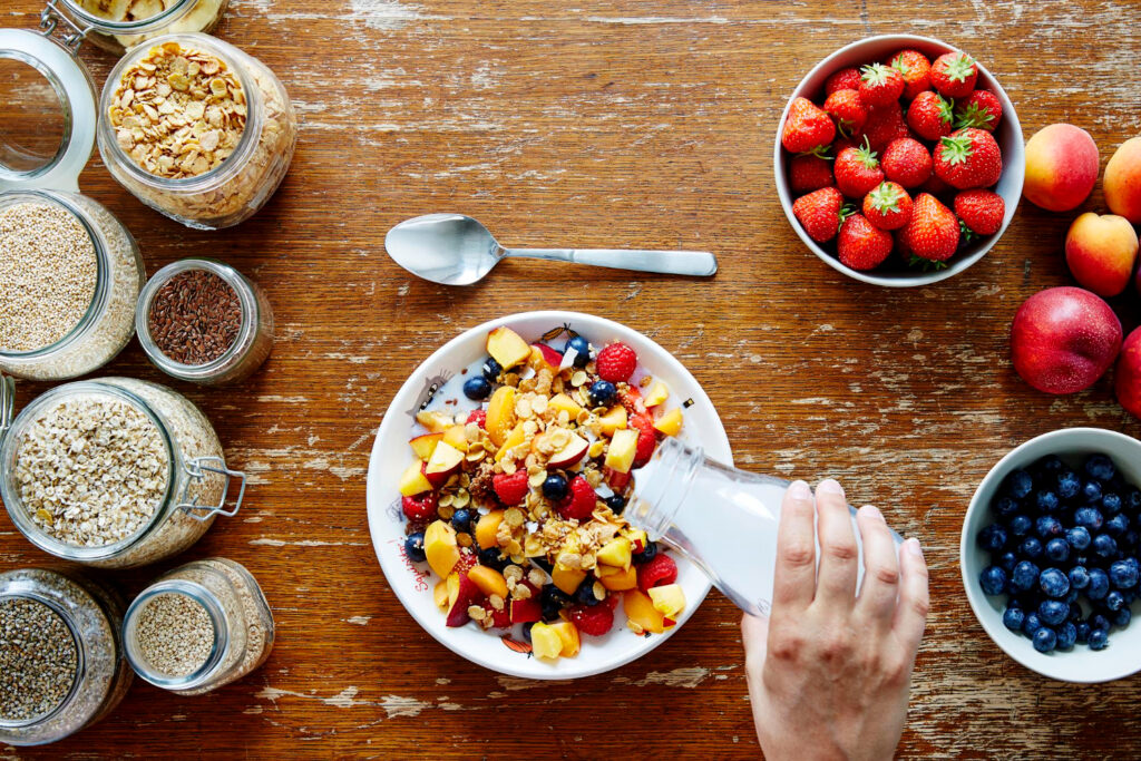 Healthy breakfast with fresh fruit, granola, oats, and milk on a wooden table