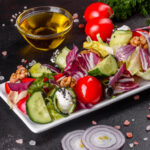 Low-carb salad with fresh vegetables, cucumbers, cherry tomatoes, black olives, walnuts, and cream cheese on a white rectangular plate