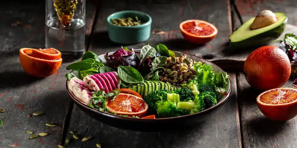 "Vibrant vegan lunch bowl with quinoa, broccoli, fresh greens, blood orange slices, and avocado"